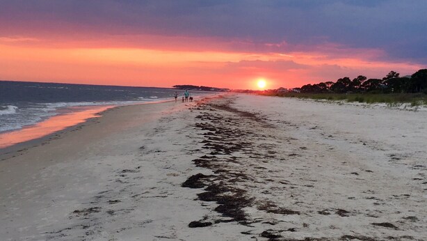 A beach at sunset with a clear sky and calm sea.
