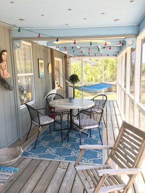 A covered patio with a round table and chairs, a hammock, and a decorative wall hanging.