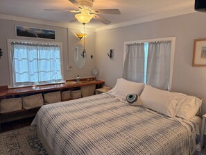 A bedroom with a bed, a vanity with a mirror, a ceiling fan, and a window with curtains.