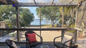 A covered outdoor seating area with wicker chairs and a small round table, overlooking a lake and trees.