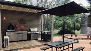 Ein Außenküchenbereich mit Grill, Spüle und Stauraumschränken, einem Picknicktisch und einem Sonnenschirm.