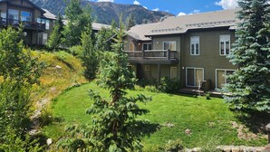 A two-story house with a balcony, surrounded by a well-maintained lawn and trees, set against a backdrop of mountains. - Snowcreek Resort Vacation Rental 954 (Mammoth Lakes)