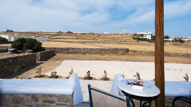 A terrace with a wooden pergola, white outdoor seating, and a view of a hilly landscape with white buildings. - Myconian Brothers    (mykonos)