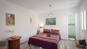 A bedroom with a bed, a bedside table, a lamp, and a painting on the wall. - Myconian Brothers    (mykonos)