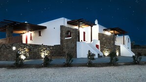 A white building with stone walls and red doors, featuring a stone staircase and a pergola. - Myconian Brothers    (mykonos)
