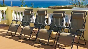 Une rangée de chaises longues sur un balcon donnant sur l’océan.
