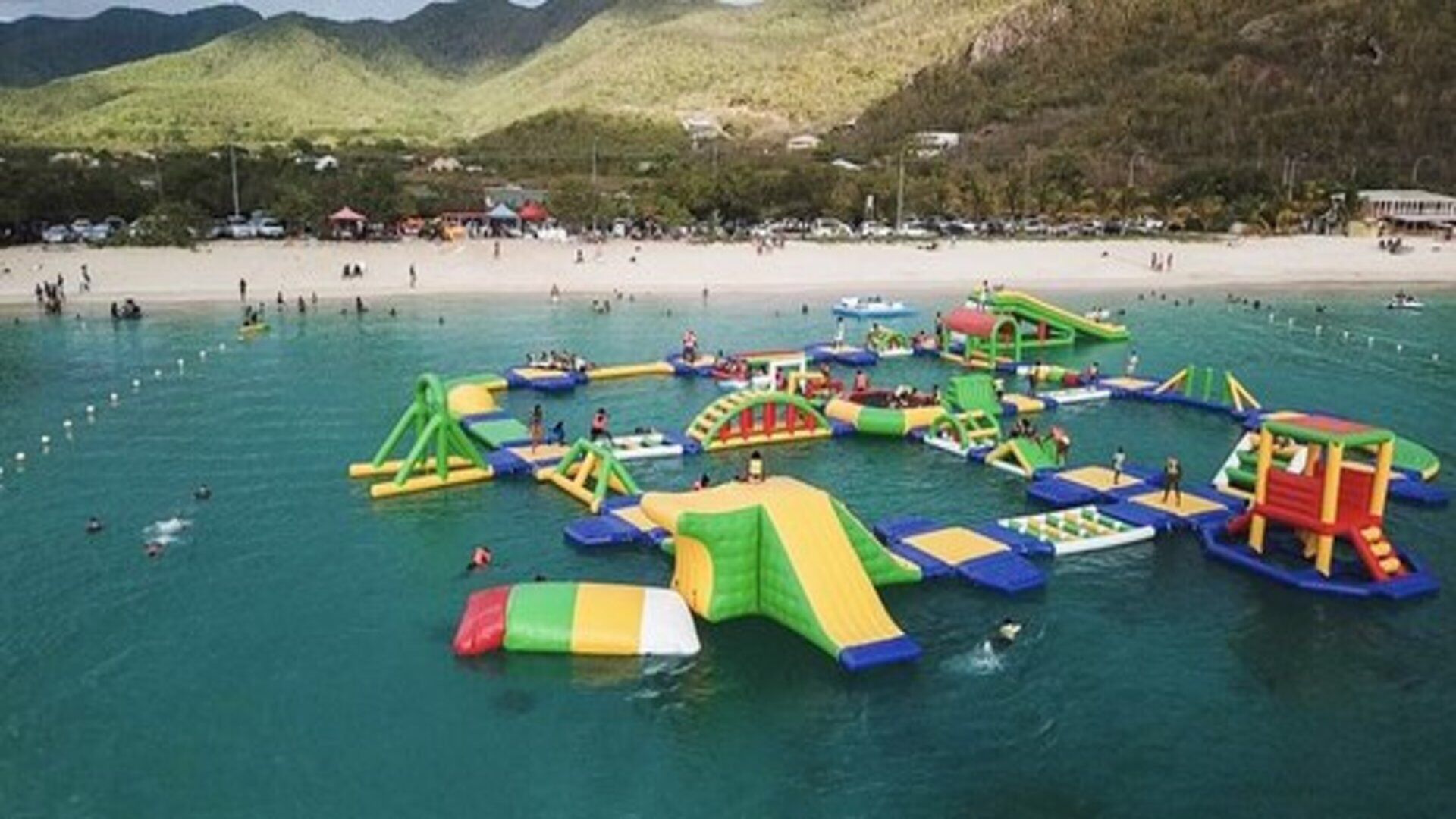 An outdoor water park with inflatable play structures and a beach in the background.