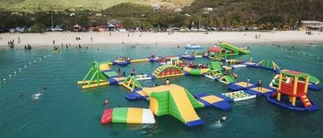 An outdoor water park with inflatable play structures and a beach in the background.
