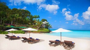 A beach with lounge chairs and umbrellas, a gazebo, and lush greenery.