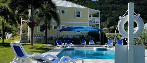 A pool area with lounge chairs, a lifebuoy sculpture, and a building with a metal roof in the background.