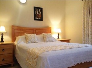 A neatly made bed with a wooden headboard, two bedside tables with lamps, and a framed picture on the wall.