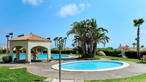 Área de piscina com um gazebo, palmeiras e um céu azul límpido.