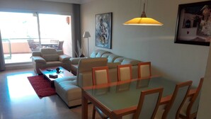 Una sala de estar moderna con una mesa de comedor de vidrio, sofás color beige y un tapete rojo.