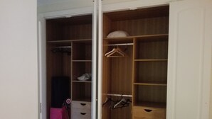 Un armario espacioso con estantes de madera, una barra para colgar y una maleta rosa.