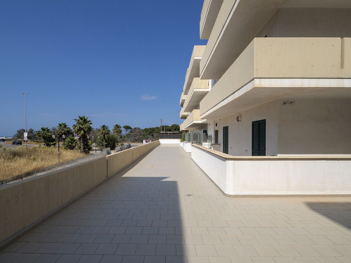 A long, straight pathway leading to a multi-story building with balconies.