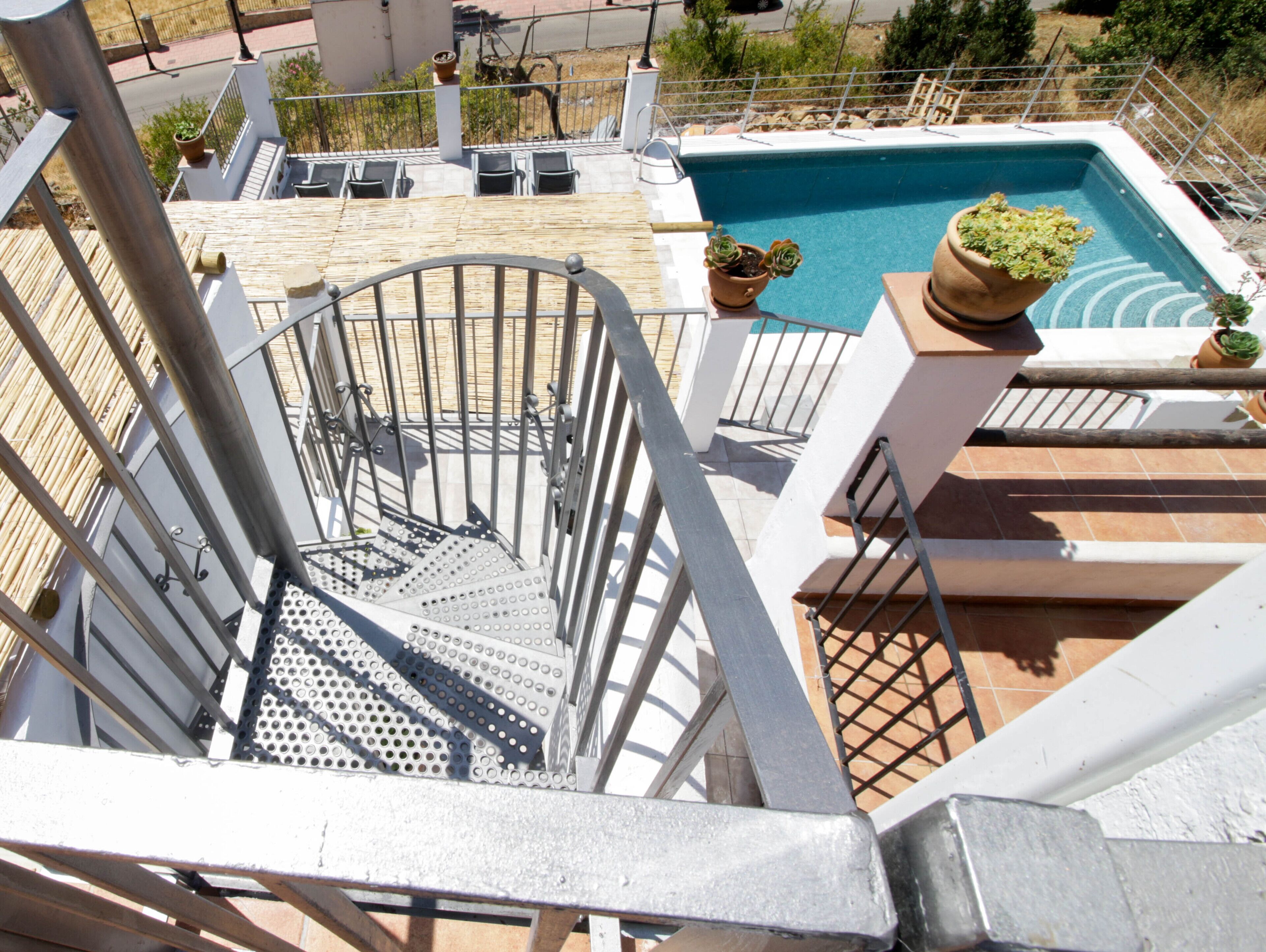 A pool area with a metal staircase leading down to a pool, surrounded by potted plants and outdoor furniture.