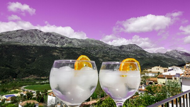 Two glasses of a clear beverage with ice and an orange slice, set against a backdrop of mountains and a village. - The best terrace of the Serranía de Ronda, Emerald Pool: Casa Martijín (Jimera de Líbar)
