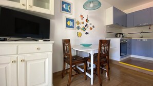 Ett modernt kök med vita skåp, ett matbord med stolar, en tv och dekorativ väggkonst med fiskmotiv.