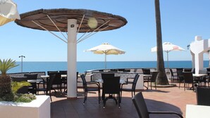 Une terrasse extérieure avec des tables et des chaises, des parasols et une vue sur la mer.