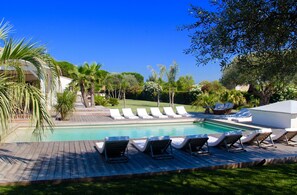 Un área de piscina con tumbonas, una terraza de madera y palmeras.