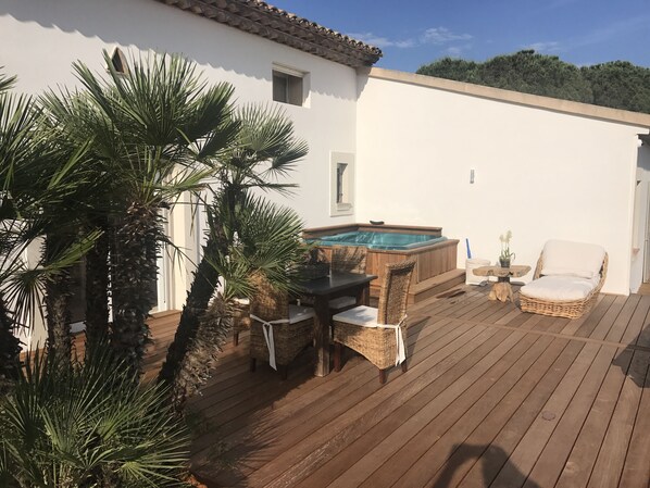 A wooden deck with a hot tub, wicker furniture, and palm trees.