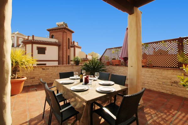 An outdoor patio with a table set for dining, surrounded by chairs, and potted plants.