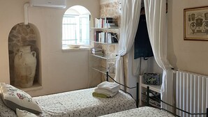Une chambre avec deux lits, un mur en pierre, une bibliothèque, un radiateur et une fenêtre avec des rideaux.