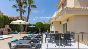 Un espace aménagé au bord de la piscine, avec des chaises longues, des parasols et une table à manger.