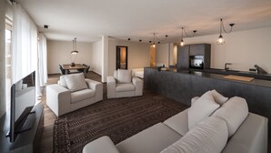Un salon moderne comprenant un canapé, des fauteuils, une table basse et un téléviseur. Il y a également un coin cuisine avec un réfrigérateur et une table à manger.