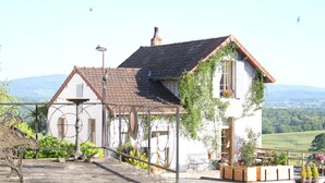 Une maison traditionnelle avec un toit en tuiles, un balcon orné de plantes en pot et une vue sur la campagne.