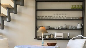 Un coin repas comprenant une table ronde, des chaises, une lampe et des étagères où sont rangés de la verrerie et de la vaisselle.