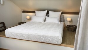 Un lit bien fait, avec un couvre-lit blanc et des oreillers, deux lampes de chevet et une tête de lit en bois.