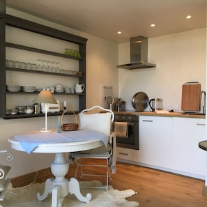A kitchen with a white countertop, a stove, and a sink. There is a shelf above the countertop holding glassware and plates. - Living on clouds in the great expanse of southern Morvan (Saint-Didier-sur-Arroux)