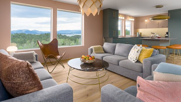 Una sala de estar moderna con un sofá, sillones, una mesa de centro y vistas a las montañas a través de grandes ventanales.