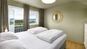 Habitación de hotel con cama, un ventanal con cortinas, un espejo redondo y vista a un paisaje montañoso.