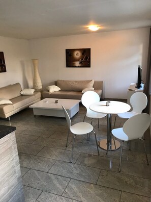 A modern living room with a sofa, a coffee table, and a dining area with chairs and a table. - Apartment in the nature reserve Schwalmtal  (Schwalmtal)