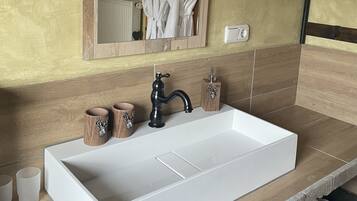 Een badkamer met een groot wit wastafel, houten wastafelmeubel en een spiegel die een badjas en een radiator weerspiegelt.