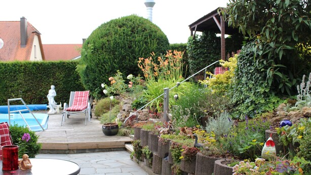 Un jardin avec un chemin en pierre, un petit bassin et un espace aménagé avec une table et des chaises.
