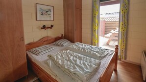 Una cama doble con cabecera de madera, un cuadro enmarcado en la pared y vistas a un patio exterior a través de una ventana con cortinas.