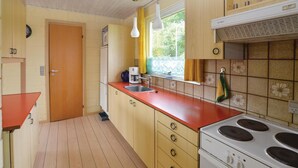 Una cocina compacta con armarios de madera, una encimera roja, un lavabo, una estufa y una ventana con cortinas.