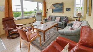 Una sala de estar con un sofá de cuero marrón, un sofá gris con cojines florales, una mesa de centro de madera y un sillón de cuero marrón.