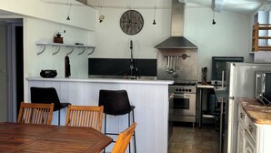 A modern kitchen with a wooden dining table and chairs, a central island, and a built-in oven. - 70m2 loft for 5 people with heated pool, village center (Sainte-Marie-De-Ré)