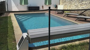 A swimming pool with a safety fence, a stone wall, and a white building with green shutters. - 70m2 loft for 5 people with heated pool, village center (Sainte-Marie-De-Ré)