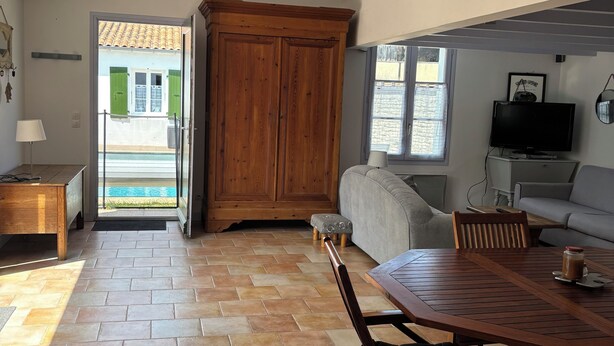 A spacious living area with a wooden dining table, a sofa, and a television. - 70m2 loft for 5 people with heated pool, village center (Sainte-Marie-De-Ré)