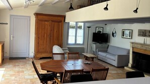 A spacious living area with a wooden dining table, a grey sofa, and a fireplace. - 70m2 loft for 5 people with heated pool, village center (Sainte-Marie-De-Ré)