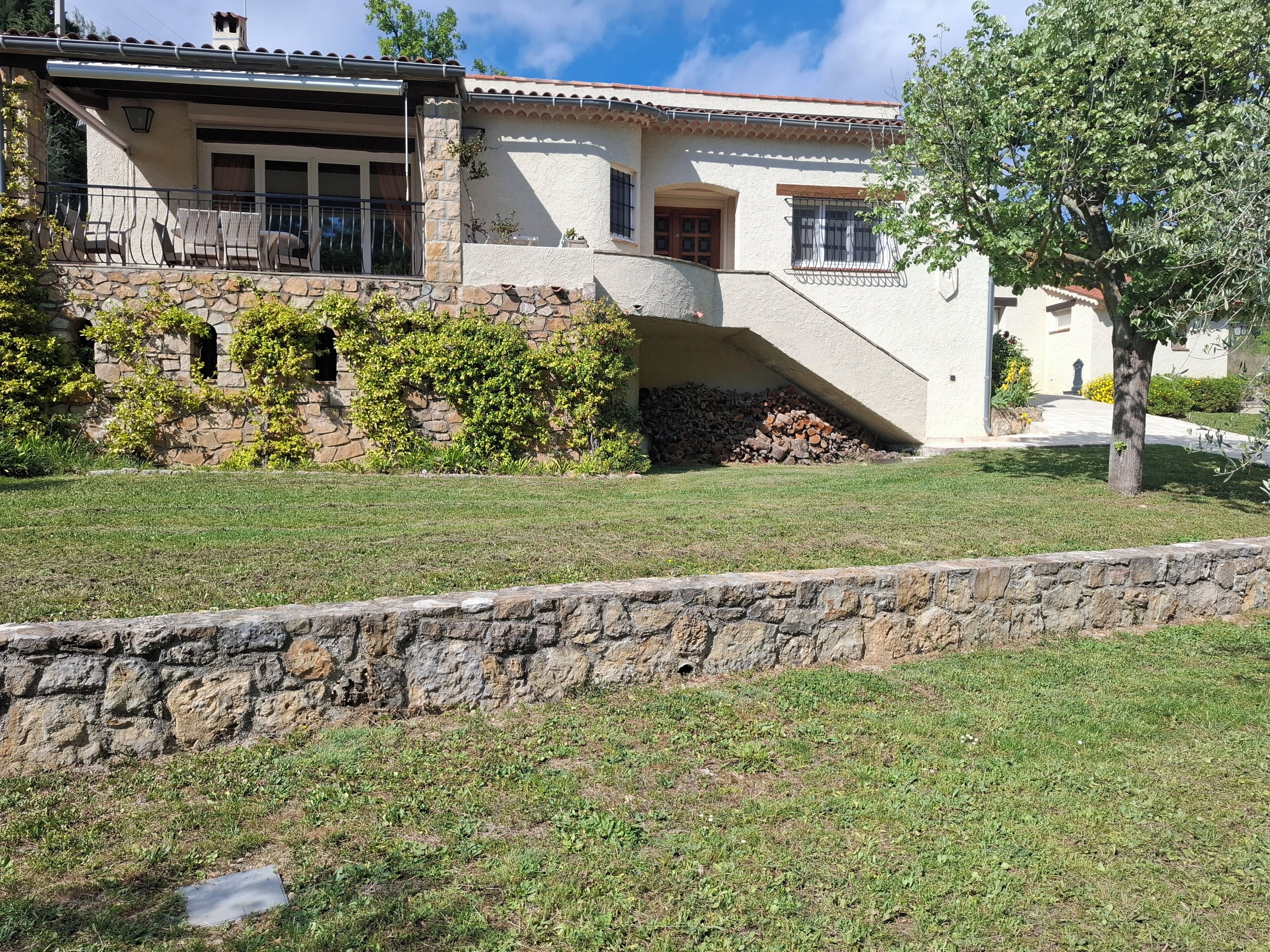 A house with a stone wall, a grassy lawn, and a tree.