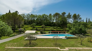 A swimming pool surrounded by a well-maintained lawn and trees, with a stone pathway leading to the pool.