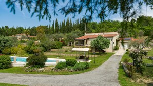 Una villa con portico coperto, piscina e giardino con diverse piante e un vialetto.