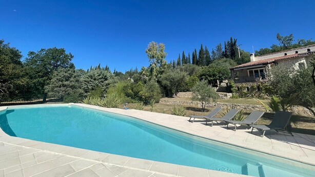 Una piscina con lettini, circondata da alberi e un edificio in pietra.