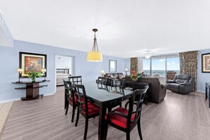 A spacious living room with a dining area, a sofa set, and a view through large windows.